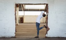Вид збоку молодої чоловічої балетної танцівниці в джинсах позує у дверях у порожній кімнаті на покинутому складі — стокове фото