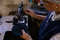 Vista lateral elevada de uma mulher de meia idade mista usando uma máquina de costura em uma fábrica de chapéus — Fotografia de Stock