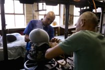 Над видом на плече старших і середнього віку змішаних чоловіків, які працюють разом на машині, що пропарює верхню частину капелюха, щоб сформувати його в майстерні на капелюшній фабриці — стокове фото