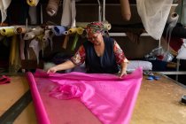 Frontansicht einer Frau mittleren Alters, die an einem faltbaren Tisch steht und in einer Hutfabrik rosafarbene Stoffbahnen misst. — Stockfoto