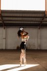 Vista lateral de uma jovem dançarina de balé feminina de raça mista vestindo sapatos pontiagudos em pé em seus dedos no eixo da luz solar enquanto dança em um quarto vazio em um armazém abandonado — Fotografia de Stock