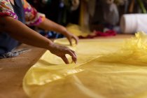 Вид збоку середня секція жінки, що стоїть за столом, працює з жовтою тканиною на фабриці капелюхів — стокове фото