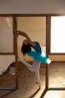 Seitenansicht einer jungen Balletttänzerin mit gemischter Rasse, die ein blaues Tutu und Spitzenschuhe trägt und mit dem Kopf auf einem Bein auf den Zehen in einem Eingang eines verlassenen Lagergebäudes posiert — Stockfoto