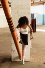 Front view close up of a young mixed race female ballet dancer wearing pointe shoes dancing standing on one leg on her toes the other leg raised on a structural pole in an empty room at an abandoned warehouse — Stock Photo
