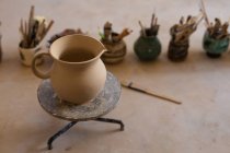 Vista elevada de uma jarra de barro em uma roda de banda sentada em um tampo de trabalho em um estúdio de cerâmica, com vasos e ferramentas no fundo — Fotografia de Stock