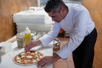 Side view close up of a middle aged Caucasian male chef carefully preparing a pizza in a restaurant kitchen — Stock Photo