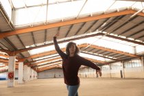Vorderansicht einer jungen gemischten Rasse Balletttänzerin in Jeans und Spitzenschuhen, die mit ausgestreckten Armen in einer verlassenen Lagerhalle tanzt — Stockfoto