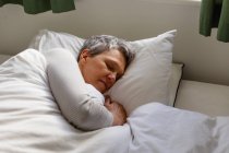 Вид сбоку на взрослую белую женщину с короткими седыми волосами, лежащую в постели дома, спящую — стоковое фото