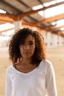 Portrait close up of a young mixed race woman with shoulder length curly hair looking straight to camera in an abandoned warehouse — Stock Photo