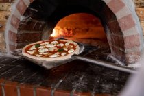 Vista frontale da vicino di una pizza su una buccia posta in un forno per pizza da cuocere — Foto stock