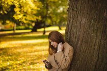 Mulher bonita usando telefone celular enquanto está de pé no parque . — Fotografia de Stock