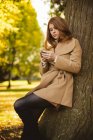 Женщина пользуется мобильным телефоном, стоя в парке . — стоковое фото