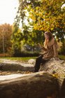 Женщина с мобильного телефона, сидя на стволе дерева в парке . — стоковое фото