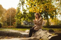 Женщина с мобильного телефона, сидя на стволе дерева в парке . — стоковое фото