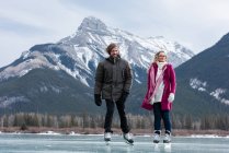 Vue de face du jeune couple caucasien patinant ensemble dans un paysage enneigé naturel — Photo de stock