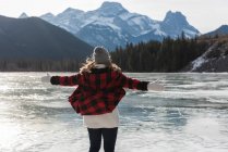 Visão traseira da mulher caucasiana feliz com o braço esticado em pé na paisagem nevada natural no fundo . — Fotografia de Stock