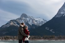 Vista lateral do jovem casal caucasiano de pé com o braço ao redor na paisagem nevada natural no fundo — Fotografia de Stock