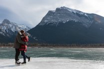 Vue latérale du couple heureux caucasien s'embrassant debout dans un paysage enneigé naturel en arrière-plan — Photo de stock