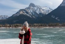 Vista frontal da bela mulher loira caucasiana vestindo roupa de inverno tendo café em pé na paisagem nevada natural — Fotografia de Stock