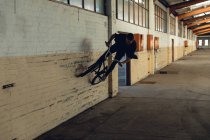 Front view of a young Caucasian man wall riding on a BMX bike in an abandoned warehouse — Stock Photo