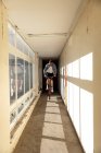 Vue de face d'un jeune homme caucasien portant des lunettes de soleil sautant sur un vélo BMX dans un couloir étroit dans un entrepôt abandonné au soleil — Photo de stock