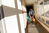 Frontansicht eines jungen kaukasischen Mannes mit Sonnenbrille, der in einem engen Korridor an einem verlassenen Lagerhaus in der Sonne ein BMX-Fahrrad mit grünen und orangefarbenen Rauchgranaten fährt — Stockfoto
