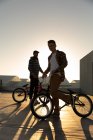 Вид збоку крупним планом двох молодих кавказьких чоловіків стояли з BMX велосипеди і на даху покинутого складу, з підсвічуванням, встановивши сонце, дивлячись на камеру — стокове фото