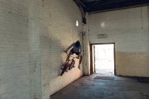 Вид спереди на молодого кавказца, скачущего на велосипеде BMX в пустом коридоре заброшенного склада — стоковое фото