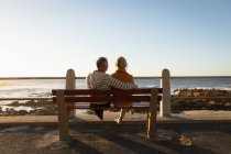 Rückansicht Nahaufnahme eines reifen kaukasischen Mannes und einer Frau, die auf einer Bank sitzen und den Blick auf das Meer bei Sonnenuntergang bewundern — Stockfoto