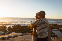 Side view close up of a mature Caucasian man and woman embracing by the sea at sunset — Stock Photo