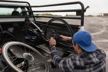 Vista trasera de cerca de un joven caucásico en silla de ruedas montando una bicicleta reclinada en un aparcamiento junto al mar - foto de stock