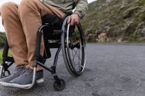 Seção baixa close up de homem em uma cadeira de rodas desfrutando de um dia em uma estrada no campo — Fotografia de Stock