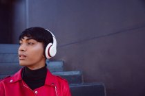 Vue latérale d'un jeune transgenre mixte à la mode adulte dans la rue, avec écouteurs allumés — Photo de stock