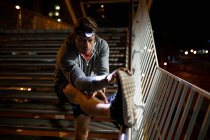 Vista frontal close-up de um jovem caucasiano que se estende em passos na rua durante o seu treino de fim de noite com um farol ligado — Fotografia de Stock