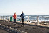 Rear view of a mature Caucasian man and woman riding e scooters by the sea — Stock Photo