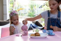 Front view of a young Caucasian girl and her tween sister having a dolls tea party at home — Stock Photo