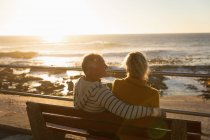 Vista posteriore primo piano di un maturo uomo e donna caucasici seduti su una panchina e ammirare la vista sul mare al tramonto — Foto stock