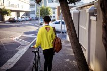Rear view of a fashionable young mixed race transgender adult in the street, walking and holding a bike — Stock Photo