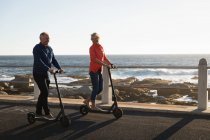 Vista frontal de um homem e mulher caucasianos maduros montando e scooters pelo mar ao pôr do sol — Fotografia de Stock