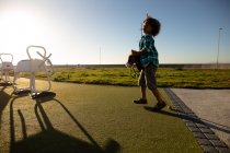 Vista laterale di un ragazzo pre-adolescente di razza mista in un parco giochi in riva al mare, che gioca con un cavallo hobby in una giornata di sole — Foto stock