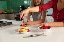 Front view close up of a young Caucasian woman making pancakes in the kitchen at home with her tween daughter — Stock Photo