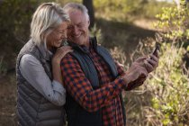 Vista lateral de um homem e uma mulher caucasianos maduros sorrindo e tirando uma selfie em um ambiente rural — Fotografia de Stock