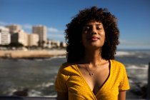 Зовнішній вигляд молодої жінки змішаної раси з закритими очима в сонячний день біля моря — стокове фото