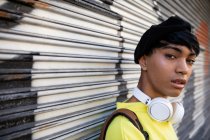 Retrato de um jovem elegante mestiço transexual adulto na rua, vestindo uma boina com graffiti no fundo — Fotografia de Stock