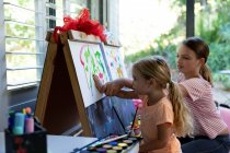 Side view of a young Caucasian girl and her tween sister painting together at home — Stock Photo