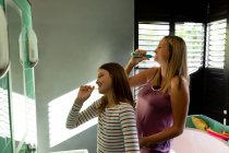 Side view of a young Caucasian pregnant woman brushing teeth with her tween daughter in their bathroom — Stock Photo