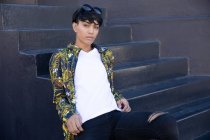 Retrato de um jovem transexual de raça mista na moda na rua, sentado em degraus por uma parede cinza — Fotografia de Stock
