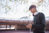 Вид збоку модного молодого змішаного гонки трансгендера дорослого на вулиці, використовуючи смартфон з навушниками на — стокове фото