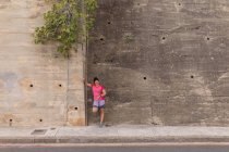 Вид на молоду Кавказьку жінку, що носить спортивний одяг, спираючись на стіну на вулиці, перевіряючи свій смарт-годинник під час роботи — стокове фото
