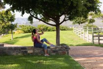 Seitenansicht einer jungen kaukasischen Frau in Sportkleidung, die während eines Workouts an einem sonnigen Tag in einem Park auf einer Mauer sitzt und Wasser trinkt — Stockfoto